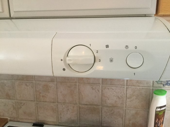 Vit kontrollpanel för köksfläkt med vred för fläkthastighet och värmeväxlingslägen.