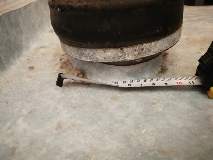 Måttband visar 90mm anslutning för toalett vid golvet, smutsig yta runtom.