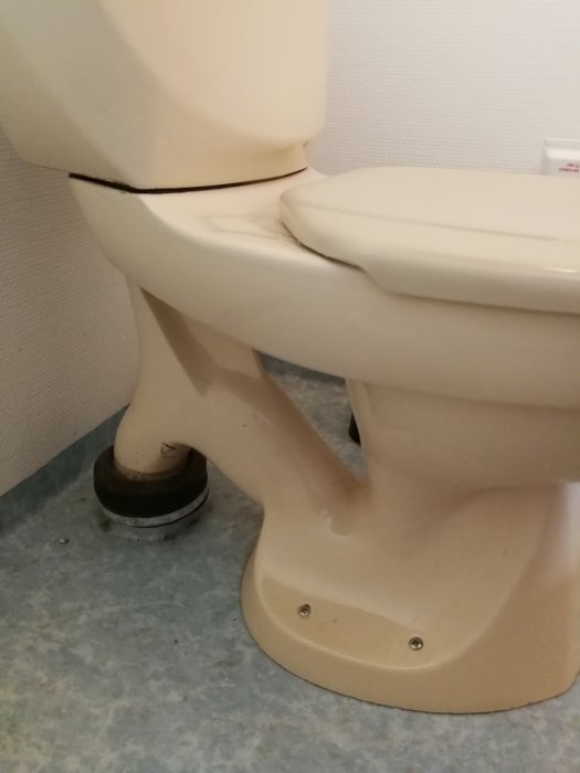 Beige toalettstol i behov av rengöring med synlig avloppsanslutning på ett fritidshus.