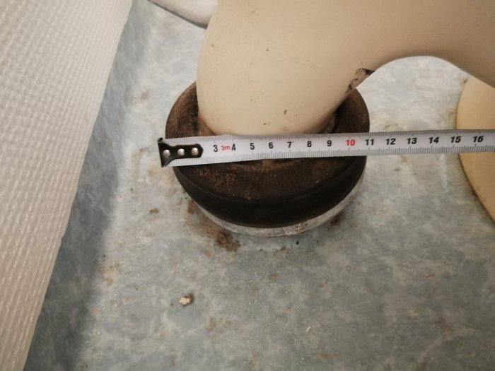 Måttband som visar diameteren på en toalettanslutning i ett badrum under renovering.