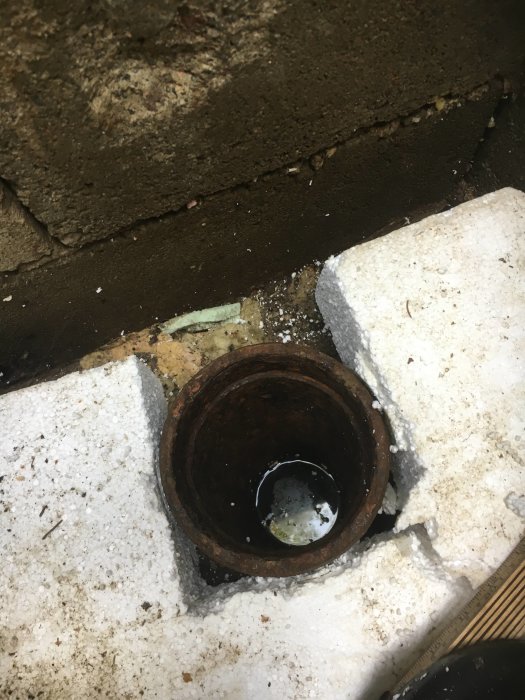Gammal brunnsöppning omgiven av isopor med lite vatten i botten, nära översvämma.