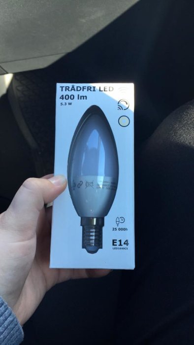 Hand håller förpackning med TRÅDFRI LED E14 spolformad ljuskälla på 400 lm och 5.3 watt.