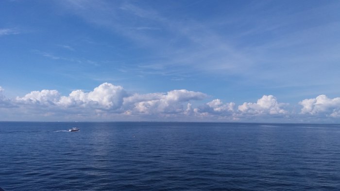 Blå himmel och vita moln över havet med en speedbåt som färdas på vattenytan.