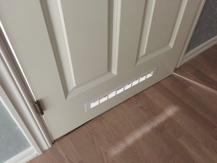Ventilationsgaller monterade på en vit innerdörr för bättre luftflöde.
