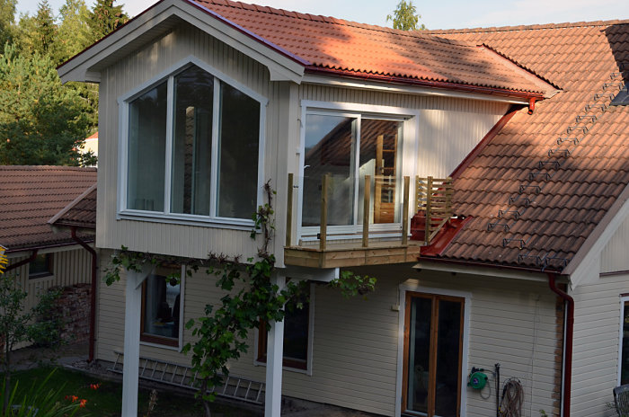 Ett nyligen renoverat hus med en nybyggd balkong och stora fönster under ett rött tegeltak i skymningsljus.