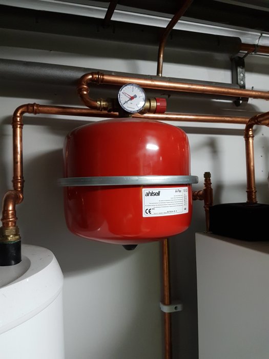 Rött expansionskärl för uppvärmning med manometer som visar lågt tryck, monterat på kopparledningar.