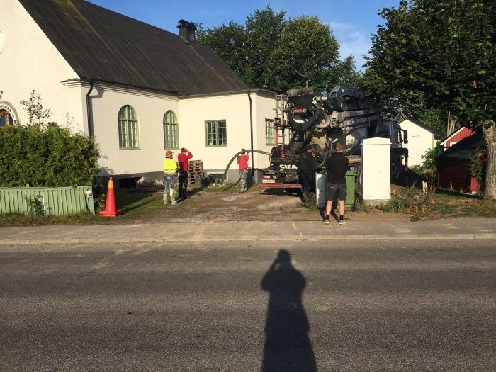 Betongbil vid hus där arbetare förbereder gjutning av betong, med säkerhetskon och träpallar.