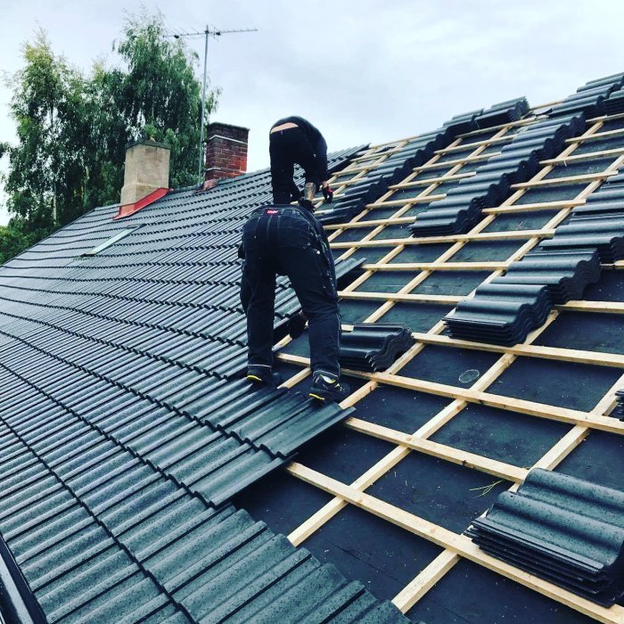Person som installerar svarta takpannor på ett takstomme under en husrenovering.