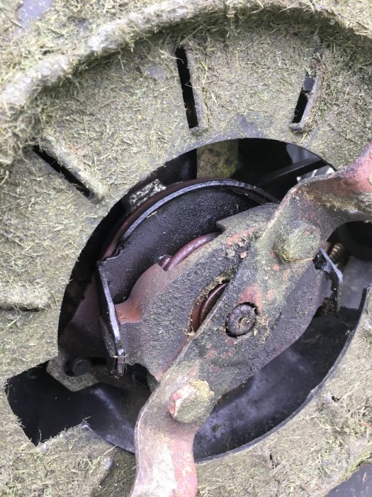 En närbild av gräsklipparblad och delar av klippaggregatet täckta av torkat gräs och smuts.