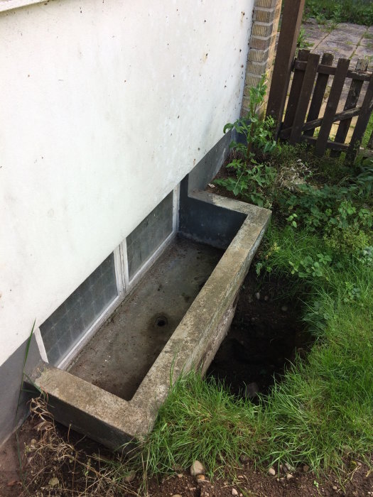 Uppgrävd ljusbrunn vid 50-talshus visar ett källarfönster och ett kort rör i betongbotten utan synligt avlopp.