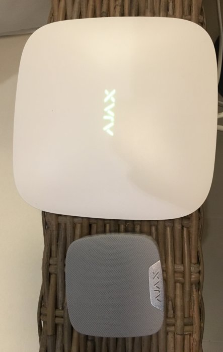 Stor vit Ajax Streetsiren ovanför en mindre grå Ajax Homesiren, båda på en rottingyta.