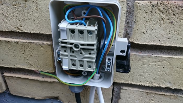 öppen elektrisk installationsdosa på en vägg med synliga ledningar och en oetiketterad trefasbrytare.