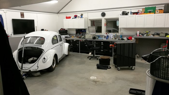 Garage med vit Volkswagen Bubbla, byggda hyllor och verktyg förberedda för billyft.