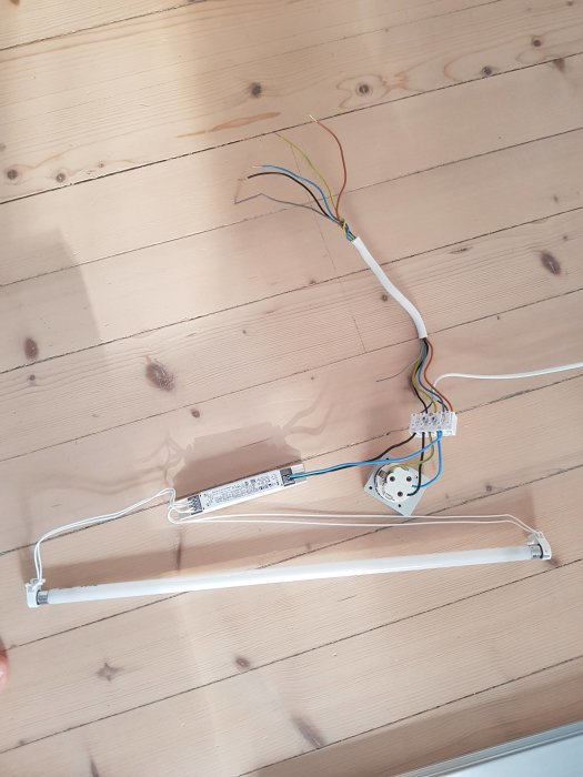 Ett öppet eluttag med fyra kablar i olika färger och en monterad ljusramp på ett trägolv.