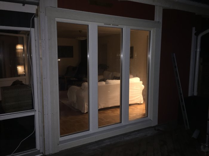 Nya fönster installerade i ett rött hus, väderskyddad utsida synlig, med inredning i bakgrunden och stege till höger.