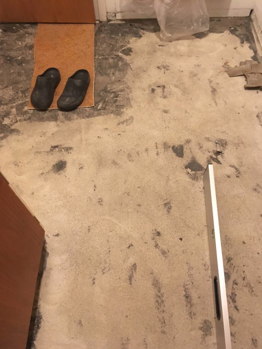 Köksgolv med borttagen plastmatta och rester av lim, skoskydd och slipverktyg synlig.