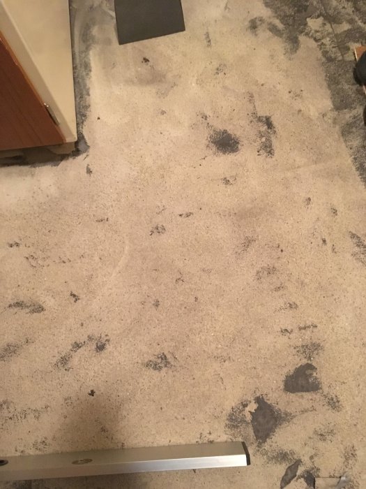 Ett köksgolv med bortriven plastmatta som visar rester av lim, främst i det vänstra hörnet.