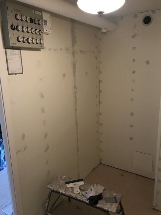 Ett rum under renovering med spacklade väggar, arbetsverktyg på en pall och en elskåpsinstallation.