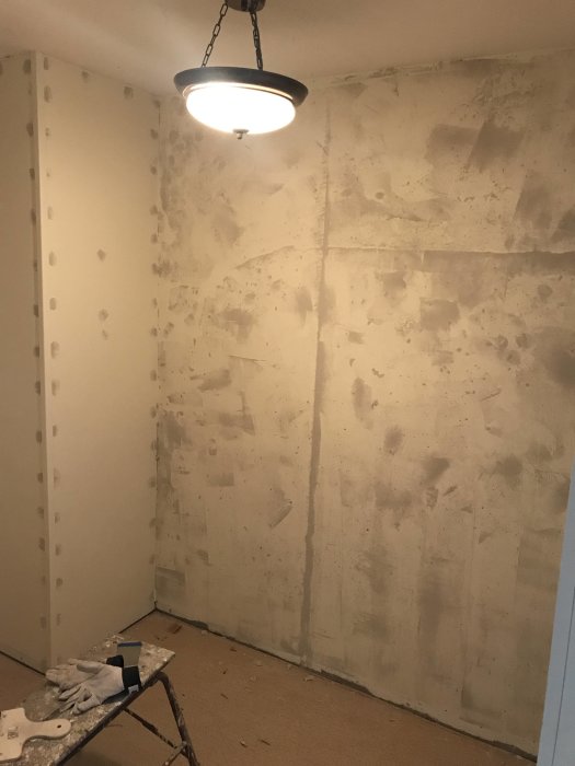 Ett rum under renovering med spacklade betongväggar och renoveringsmaterial synligt.