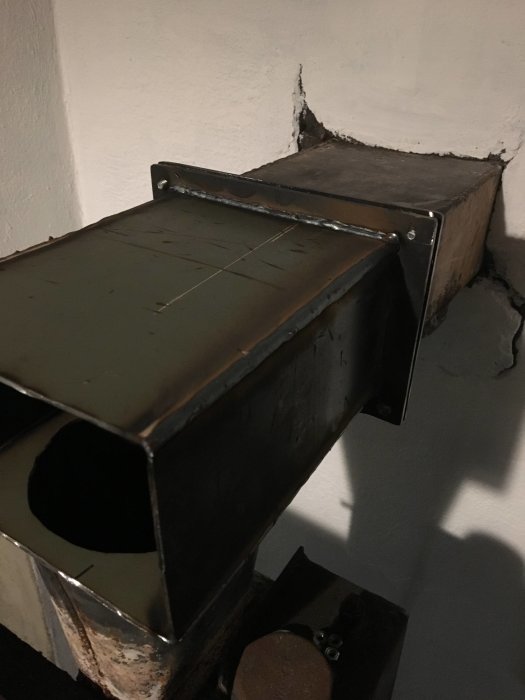 Provmonterad mellandel för rökrör av 3mm plåt vid inmurad stos, med oidentifierat lock i hörnet.