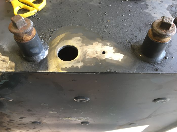 Svetsade förstärkningar och nya hål i metallpannan, vissa pluggade, med verktyg synliga.