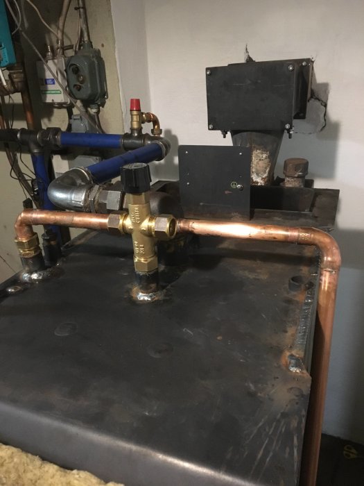 VVS-installation med kopparledningar och ventiler på en svart panna, nylagade hål synliga.