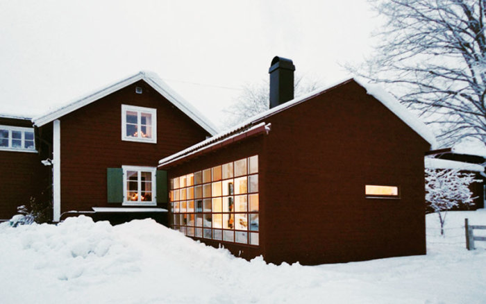 Tillbyggnad med modern stil på ett gammalt rött torp, stora fönsterpartier med snö runtomkring.