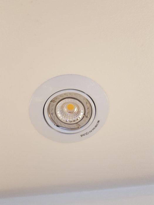Inbyggd takspotlight i vit färg med LED-lampa och text på kanten.