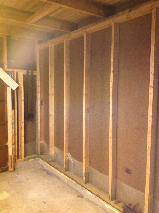 Frilagd isolerad garagevägg av träreglar och fiberplattor, redo för ytterligare renovering.