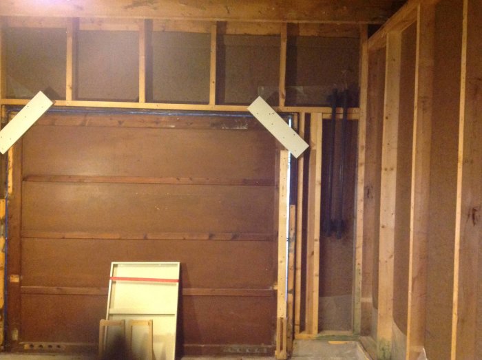 Frilagd vägg i garage under renovering med synliga stolpar och en garageport redo för isolering.