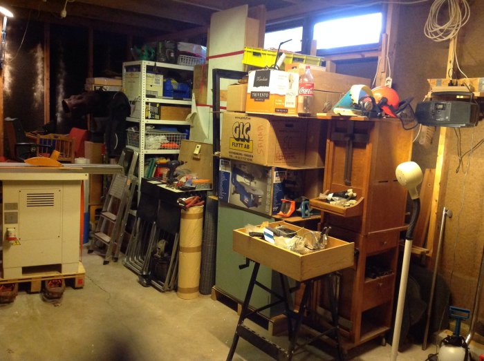 Ett rörigt garage med verktyg, lådor och föremål utspridda över arbetsbänkar och hyllor.