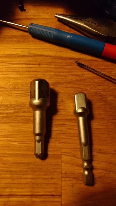 Avbruten bitshållare till hylsadapter bredvid intakt adapter, skruvmejsel och tång på arbetsbord.