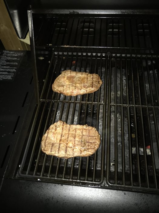 Två stycken grillade biffar på grillgallret i en öppen grill.