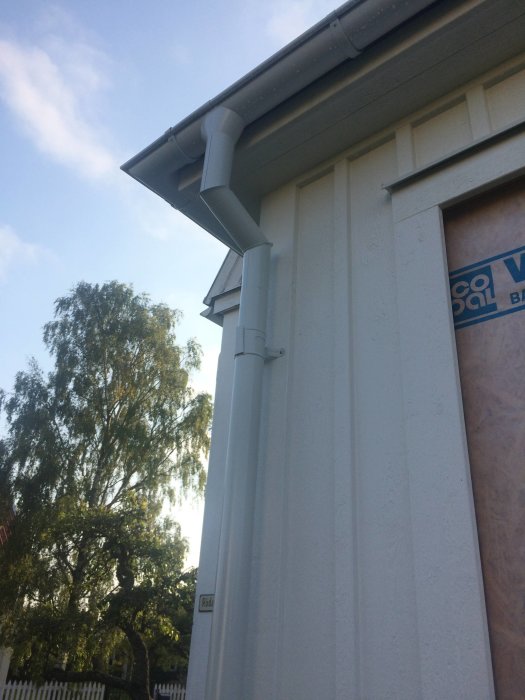 Nyligen installerad takavvattning och stuprör vid husets hörn mot en klar himmel.