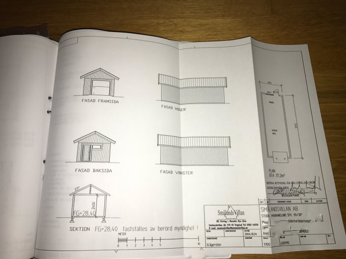 Ritning på garage med mått och olika fasadvyer öppnad på ett bord.