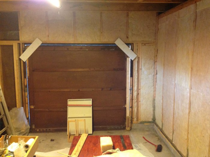 Isoleringsarbete i ett garage med synliga isoleringspaneler på en vägg och en garageport.