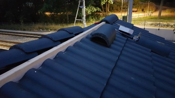 Tak i skymningen med nockbräda och nockpannor installerade, stege och verktyg synliga.
