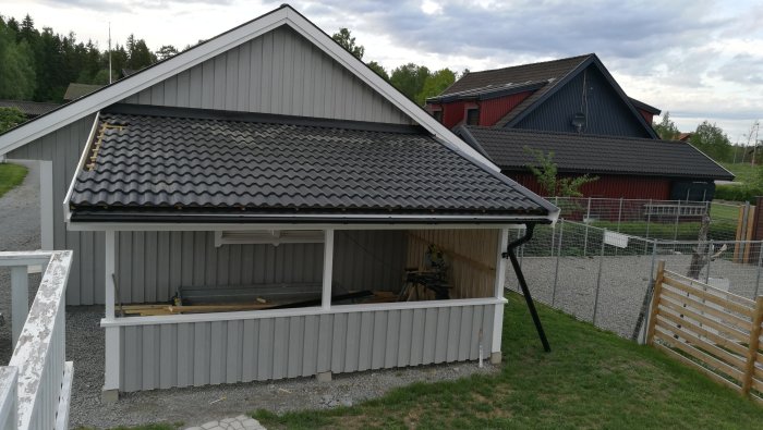 Nybyggd carport med ljust trä och ommålad, grå panel, intill ett garage.
