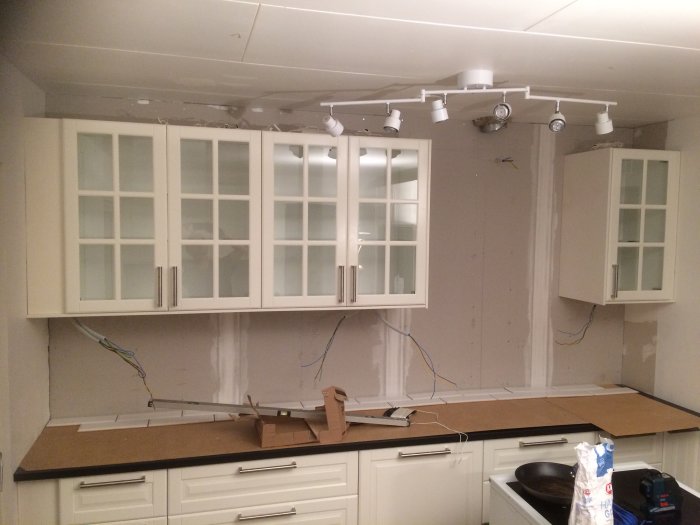 Kök före kakling med vita skåp, avskalade väggar och elektriska ledningar som framträder.