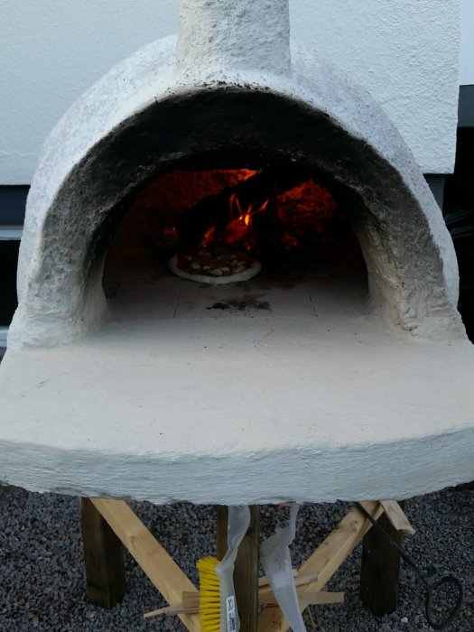 Utomhusugn av vermikulitbetong utan isolering med öppen eld och pizza inuti, på en tillfällig träställning.