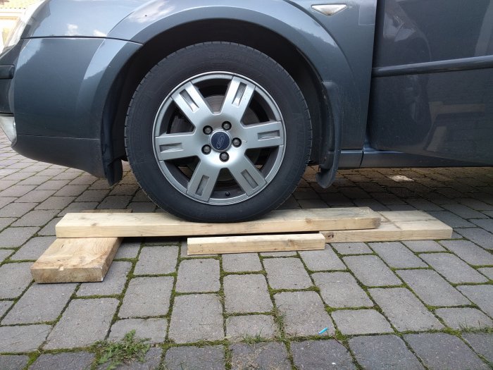 Bilhjul på enkla träramper av plankor placerade på asfalterad mark.