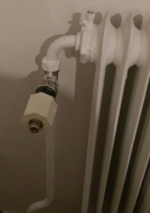 Bild på en vit radiator med anslutningsventil, detaljvisning av anslutningsrör och termostat.