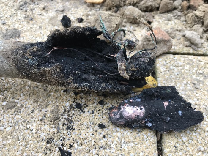 Avbränd elektrisk kabel med svartned och skadad isolering som ligger på en stenbelagd yta.