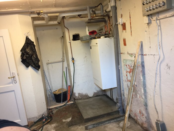 Källarförråd under renovering med VVS-rör, elskåp och avskalade väggar.