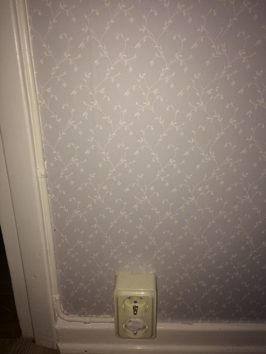 Strömbrytare ovanför ett vägguttag mot en tapet med lövmönster, behov av installation av dimmer.