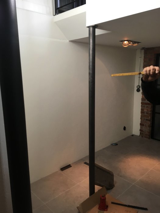 En person mäter avståndet kring en trappstolpe i ett pågående renoveringsprojekt.