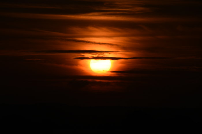 En dramatisk solnedgång med rika orange och röda toner där solen sjunker ner bakom molnen.