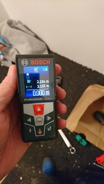 Hand håller en Bosch GLM 50 C laseravståndsmätare med mätvärden på skärmen.