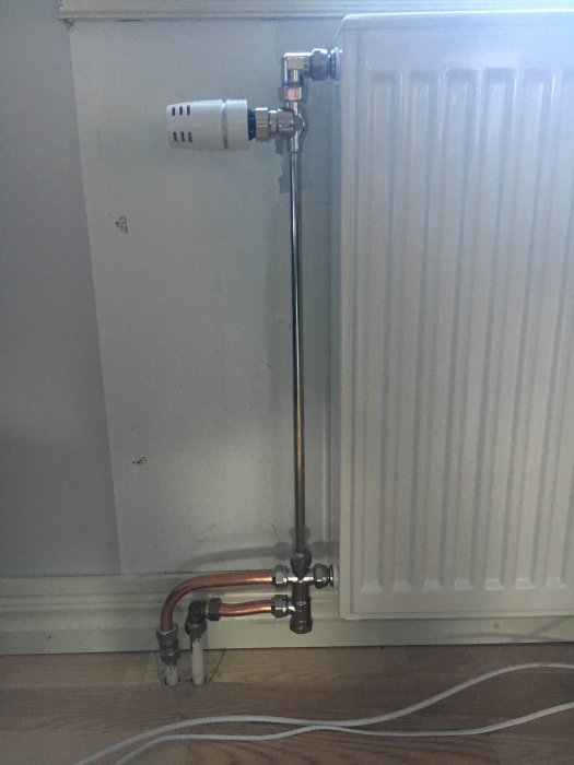 Radiatorkoppling i ett rum med synliga kopparrör och termostat.