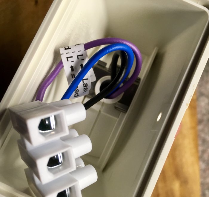 Närbild på en rörelsevakts inre med kablar och terminaler, inklusive en lila ledning som kan vara skyddsjord.